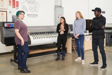 Graphic and Print Technician students standing in front of a printing press.