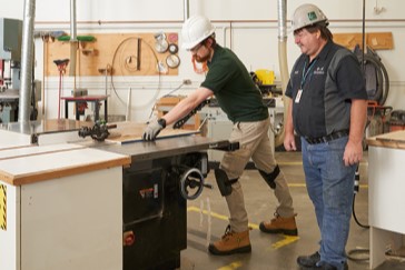 Carpentry students running a piece of wood through a table saw.